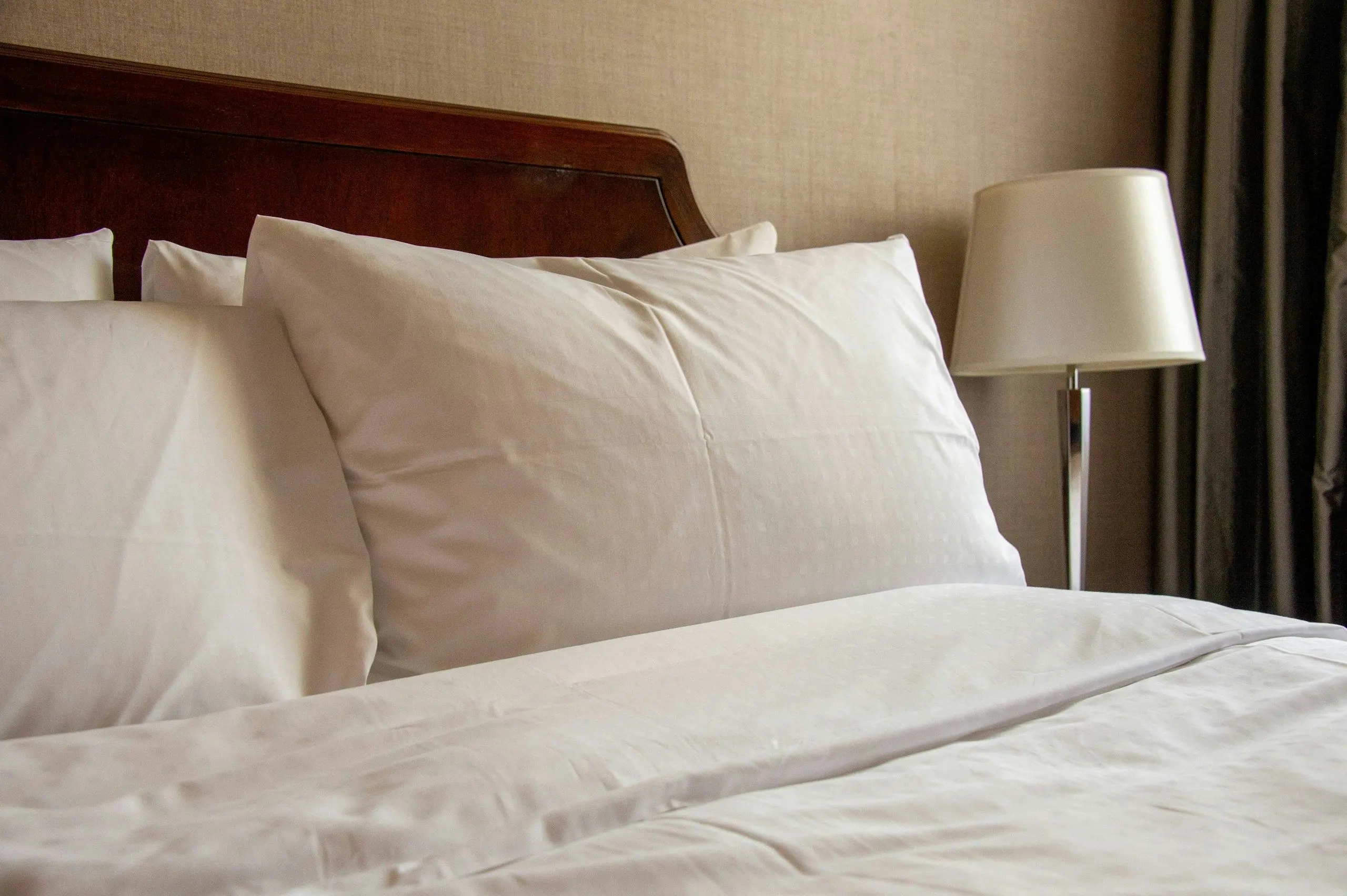 Close-up of a freshly made bed with white pillows beside a bedside lamp