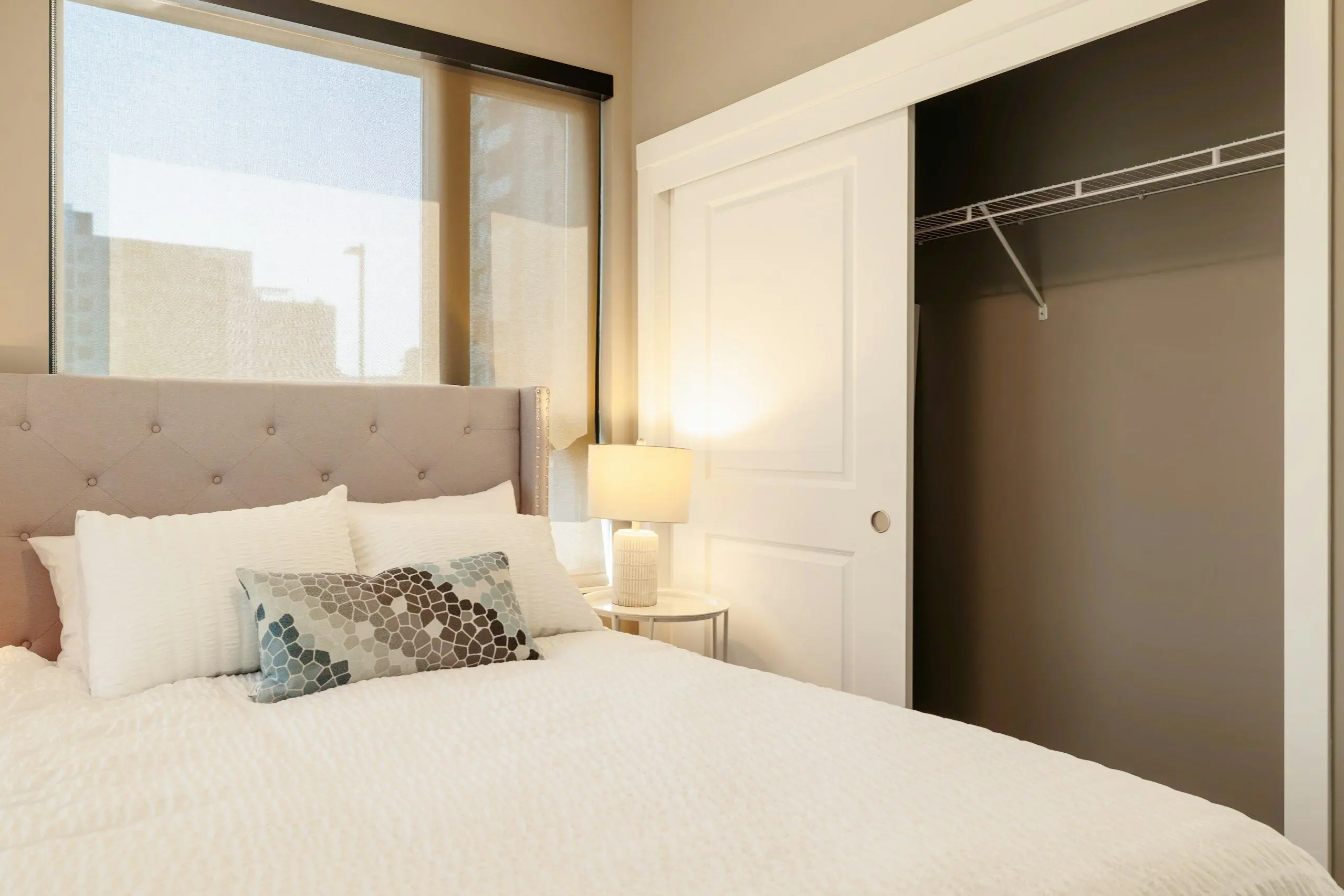 A neatly made bed with a padded headboard and bedside lamp