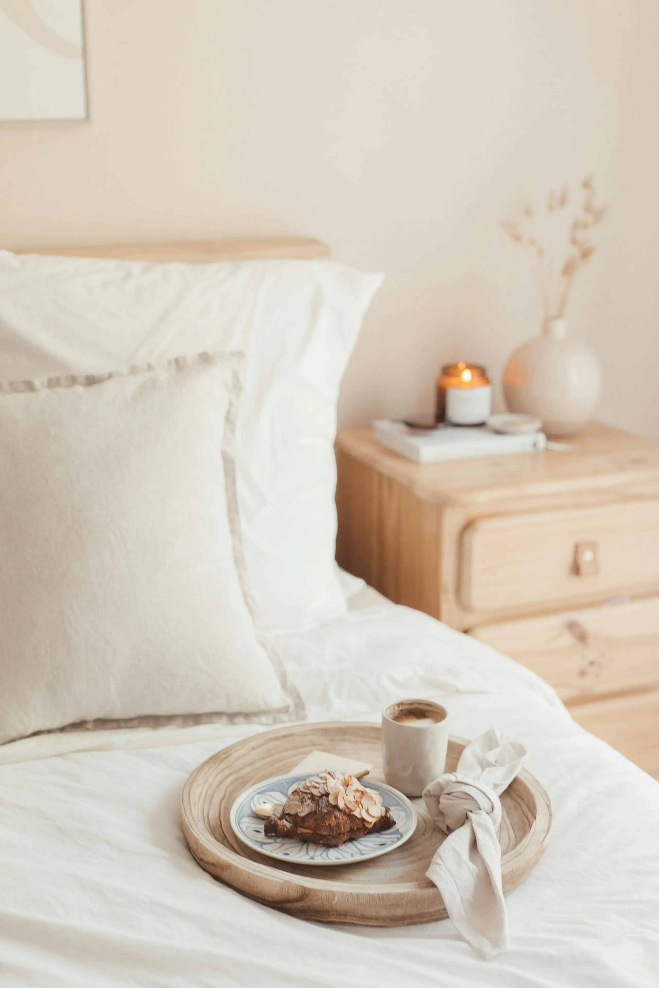 A white mug on a bedside table beside a freshly made bed